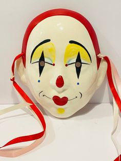 a white mask with yellow and red painted on it's face next to a red ribbon