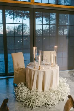 a table with candles and flowers on it in front of a large window at night