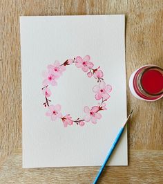 a watercolor painting of a pink flower wreath next to a cup of red liquid