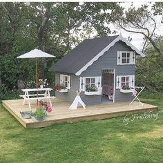 a small gray house sitting on top of a wooden deck next to flowers and an umbrella