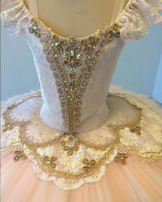 the back of a ballerina's dress is adorned with gold and crystal beads