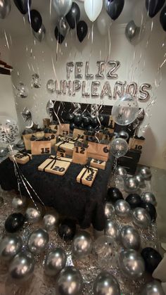 a table topped with lots of black and silver balloons in front of a sign that says feliz cumpleions