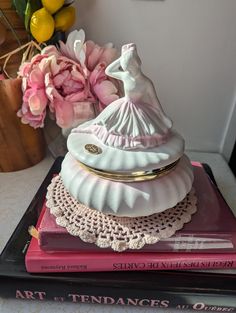 there is a figurine that is on top of some books and pink flowers