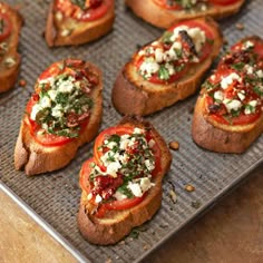 small toasted breads topped with tomatoes and feta cheese on a baking sheet