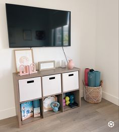 a flat screen tv mounted on the wall next to toy bins and baskets in front of it