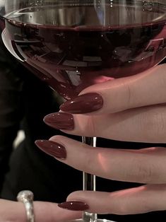 a woman's hand holding a wine glass with red nail polish on the tip