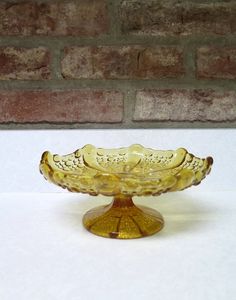 a yellow glass bowl sitting on top of a white table next to a brick wall