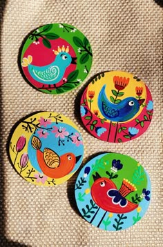 three colorful bird coasters sitting on top of a piece of cloth next to each other