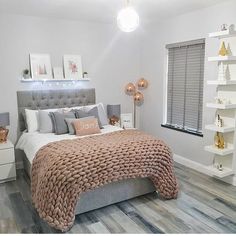 a bedroom with white walls and wood flooring is decorated in pink, grey and gold