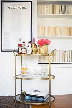 a bar cart with bottles and glasses on it in front of a bookshelf