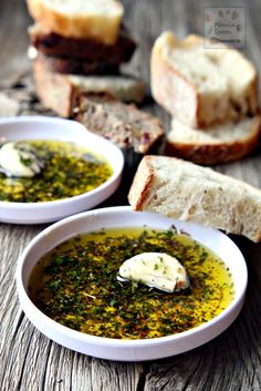 two white bowls filled with pesto and bread on top of a wooden table next to slices of bread