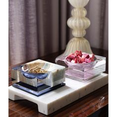 two glass dishes on a marble tray next to a white vase with flowers in it