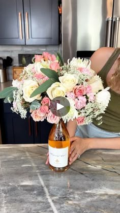 a woman is holding a bouquet of flowers and a bottle of wine on the kitchen counter