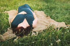 a woman laying on top of a blanket in the middle of a grass covered field