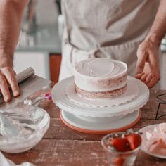 a person cutting a cake on top of a wooden table next to other plates and utensils