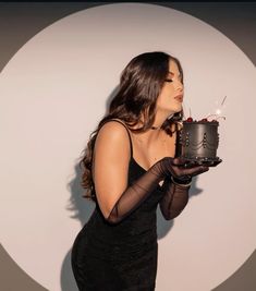 a woman holding a cake with candles in her mouth and wearing black gloves on the other hand