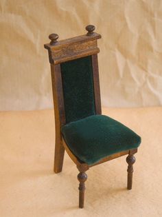 a miniature wooden chair with green velvet seat and back rest on a beige background,