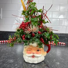 a ceramic santa claus planter with red berries and greenery on it's head