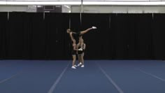 two women are doing acrobatic tricks on a blue floor in front of a black curtain