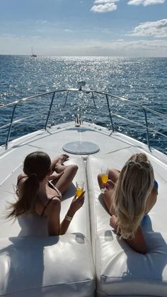 two women sitting on the back of a boat with drinks in their hands and looking out at the ocean