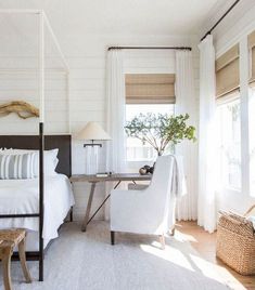 a bedroom with white walls and wood flooring has a canopy bed, two chairs, and a small table with a potted plant on it