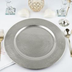 an empty silver plate on a white table cloth with gold utensils and napkins