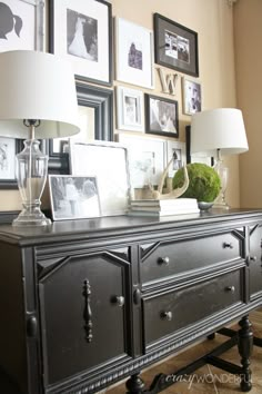 a dresser with pictures on the wall behind it and two lamps in front of it