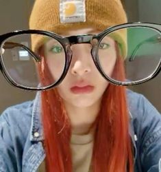 a woman with red hair wearing glasses and a beanie on top of her head