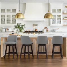 three bar stools sit in front of an island with marble countertops and gold pendant lights