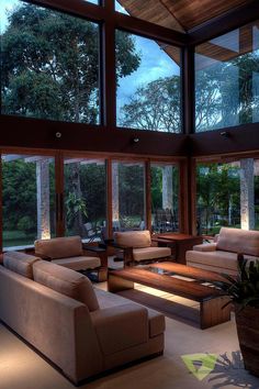 a living room filled with lots of furniture and large windows overlooking the forest at night