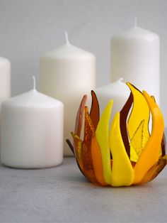 three candles sitting next to each other on top of a white table with orange and yellow decorations