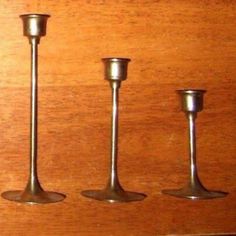 three metal candlesticks sitting on top of a wooden table