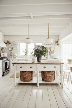 a kitchen with white walls and floors has two baskets on the island in front of it