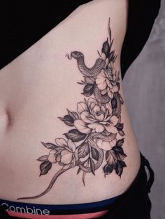 a woman's stomach with flowers and a snake tattoo on her side ribcage