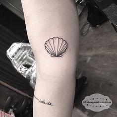 a black and white photo of a shell tattoo on the right arm with words written below it