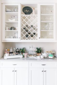 a kitchen with white cabinets and shelves filled with wine bottles, glasses and other items