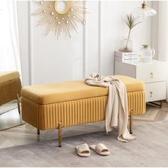 a yellow bench sitting in front of a window next to a pair of slippers