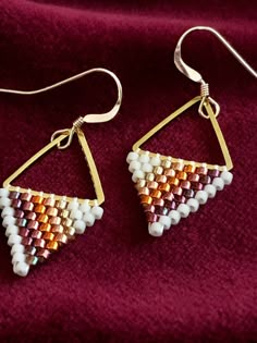 a pair of earrings with white and gold beads hanging from them on a red velvet surface