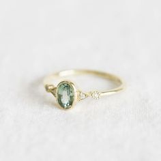 a gold ring with an oval green stone and two small diamonds on the side, sitting on a white surface