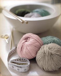 three balls of yarn are next to a measuring tape and a ball of knitting needles