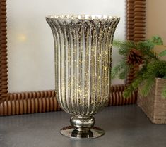 a large glass vase sitting on top of a table next to a potted plant