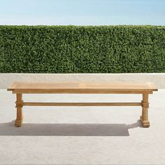 a wooden bench sitting in front of a green hedge covered wall and concrete flooring