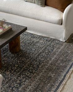 a white couch sitting next to a wooden table on top of a blue and beige rug