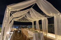 an outdoor wedding setup with white draping and string lights on the roof top