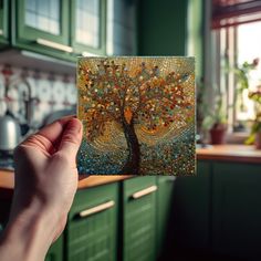 a person holding up a piece of art with a tree on it