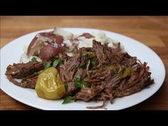 a white plate topped with meat, potatoes and green peppers on top of a wooden table