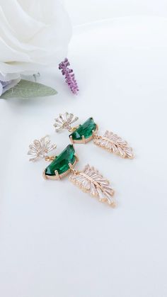 two pairs of earrings with green stones and leaves on the front, one is gold