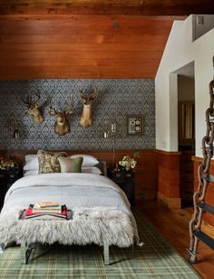 a bed room with a neatly made bed and two deer head mounted to the wall