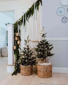 two small christmas trees in baskets next to a banister with greenery on it