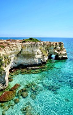 an ocean cliff with clear blue water and people standing on it